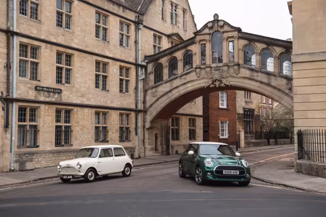 Bílé původní Mini a zelené moderní MINI stojí před historickými budovami v Oxfordu